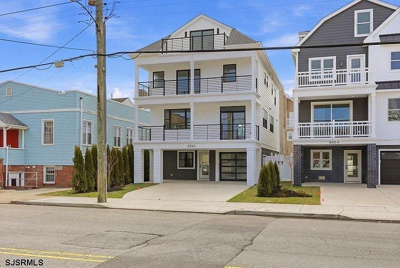 Daytime front elevation of 6302 Ventnor Avenue showing three balconies, white siding, and the central front entrance